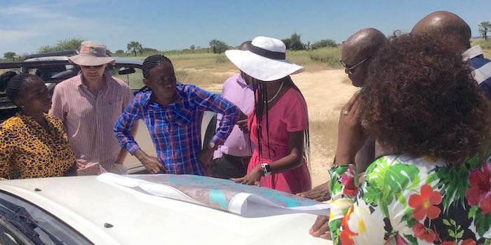 A group of people discuss an urban planning map laid on the bonnet of a vehicle..